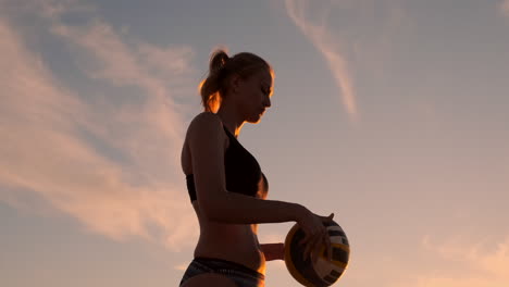 Eine-Schöne-Frau-Im-Bikini-Mit-Einem-Ball-Macht-Sich-Bei-Sonnenuntergang-Bereit,-Bei-Einem-Volleyballspiel-Im-Sand-Am-Strand-Einen-Aufschlagsprung-Zu-Machen.-Der-Entscheidende-Moment,-Der-Spannende-Moment-Des-Spiels-In-Zeitlupe.